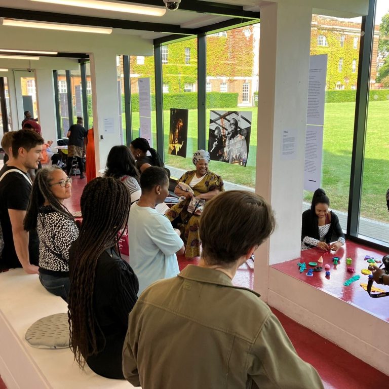 Workshop led by Damali Ibreck, (Routing Diaspora Histories, 2024) A group of people engaged in an art exhibition in a bright gallery space.